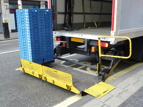 Hydraulic liftgate on a delivery truck being used to unload blue plastic crates onto the street.