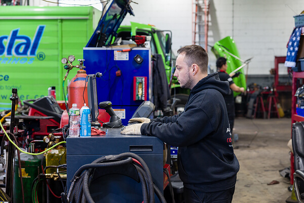 Auto technician at TLC Auto & Truck Repair working on a computer diagnostic system in a truck repair shop.